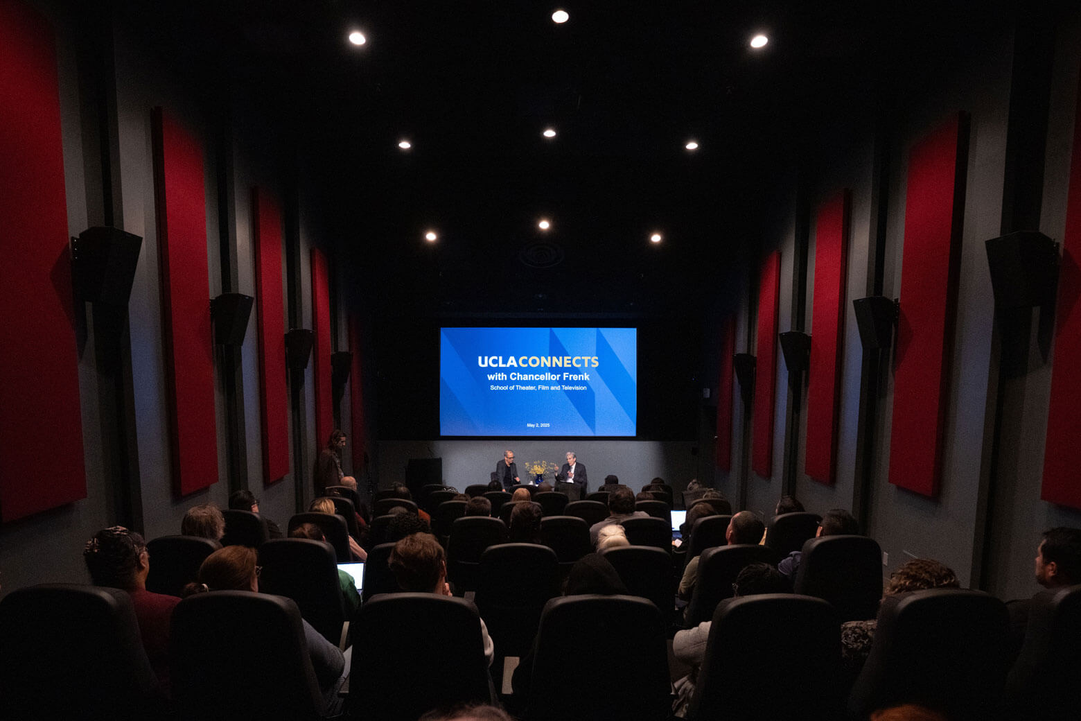 UCLA Chancellor Frenk sitting in a theater talking to audience with UCLA Connects projected on the screen.