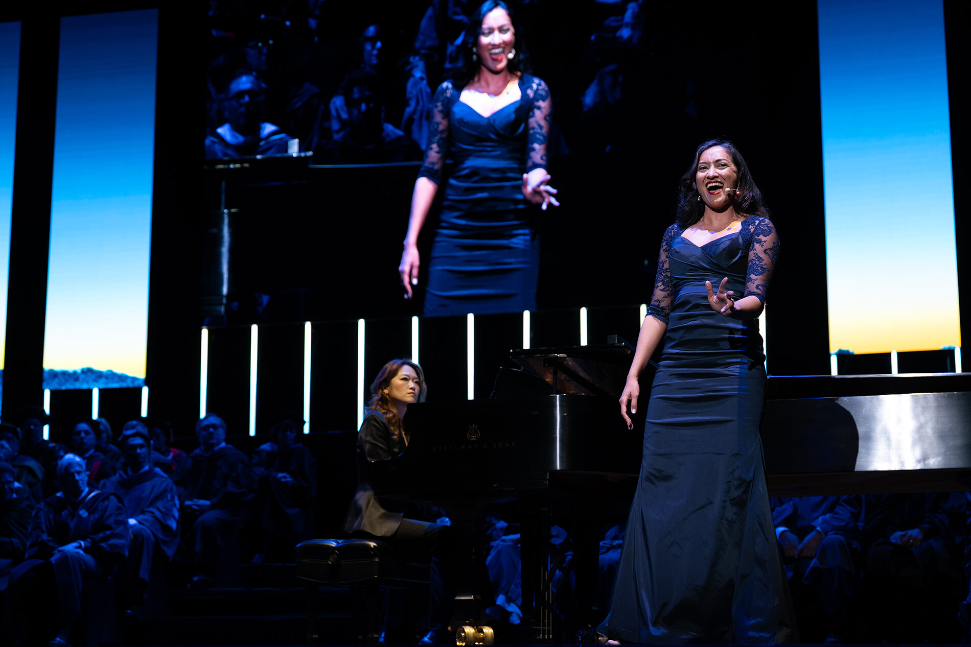Opera UCLA Performer Leela Subramaniam in dark blue dress with lace sleeves, singing onstage with pianist Sky Lee behind her