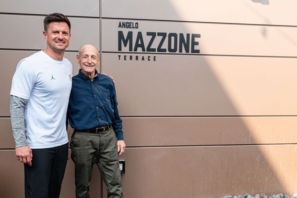 Bob Chesney (left), in white T-shirt and black pants standing next to Angelo Mazzone, in dark-blue button down and gray slacks, next to Angelo Mazzone Terrace sign