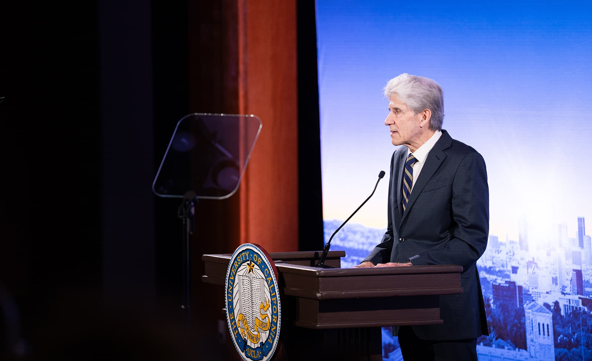 A profile shot of UCLA Chancellor Julio Frenk standing at a lectern with a microphone.