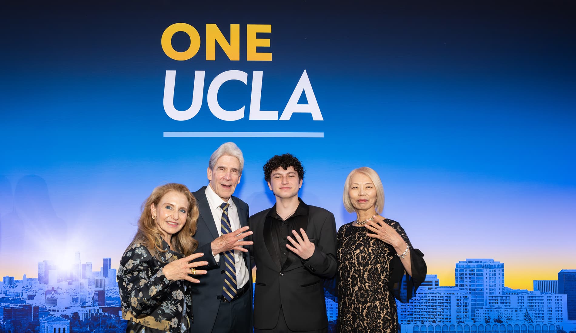 Felicia Knaul and UCLA Chancellor Julio Frenk stand with two others in front of a One UCLA backdrop holding up four fingers.
