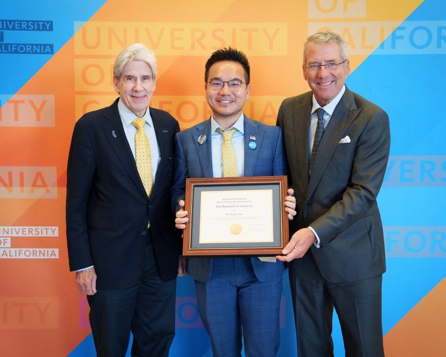 From left: Julio Frenk, Jack Feng and James B. Milliken in business attire, posing with a framed University of California award certificate against a blue-and-gold University of California backdrop, smiling for a presentation photo.